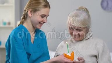 微笑的医务工作者给快乐的老年妇女带来了带蜡烛的松饼，b日